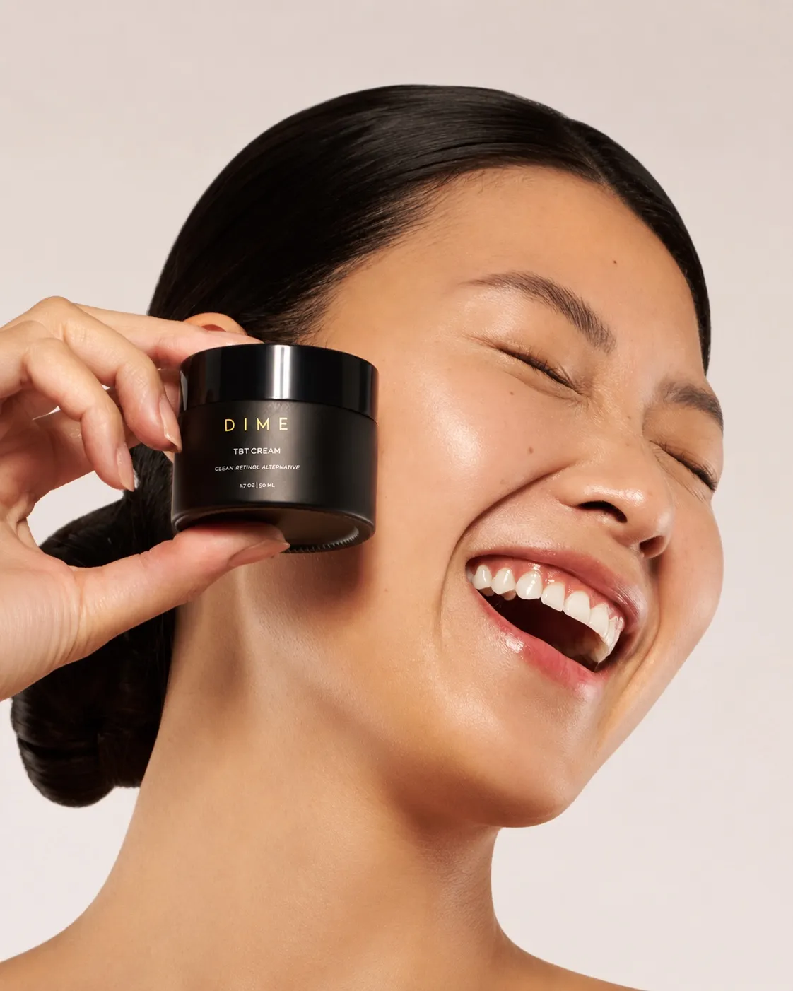 A person smiling and holding a jar of DIME Beauty TBT cream beside their face
